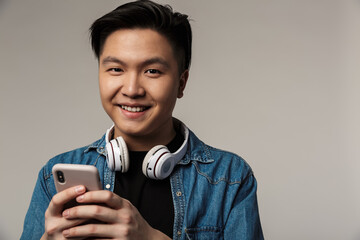 Image of smiling asian man using smartphone and wireless headphones