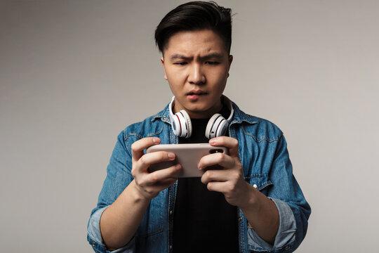 Image of unhappy young asian man playing video game on smartphone