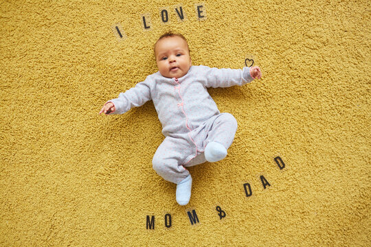 Top Down Portrait Of Cute Mixed-race Baby Lying On Fluffy Yellow Carpet With Words I Love Mom And Dad, Copy Space