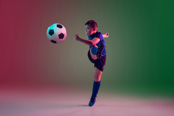 Fototapeta na wymiar Emotions. Teen male football or soccer player on gradient background in neon light. Caucasian boy training, practicing on the run, in jump. Concept of sport, competition, winning, motion, action.