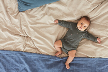 Top down view at cute mixed-race baby lying on comfortable bed with fluffy blue and white blankets,...