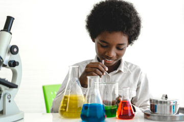 African american cute little boy student child learning research and doing a chemical experiment while making analyzing and mixing  liquid in glass at science class on the table