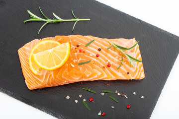 Fresh raw salmon fillet with rosemary and lemon. Salmon steak with seasonings on black plate.