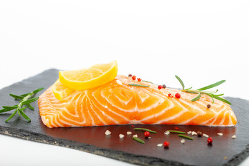 Fresh raw salmon fillet with rosemary and lemon. Salmon steak with seasonings on black plate.