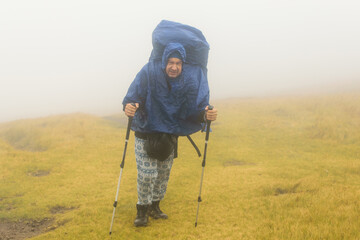 A man hiker in a rain cover in the fog during bad weather.