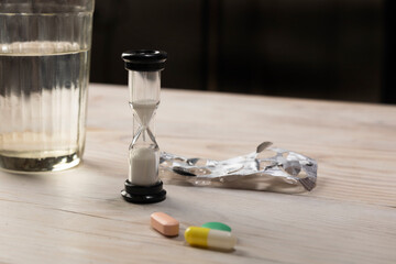 Hourglass, pills and glass of water on wooden table. Selective focus. Time-dependent survival medicine and medical.