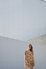 Outdoor portrait of stylish fashionable woman in colorful dress in front of a grey wall. Casual summertime hippie boho outfit, spring-summer fashion trend.