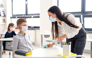 Teacher and children with face mask back at school, disinfecting desks.