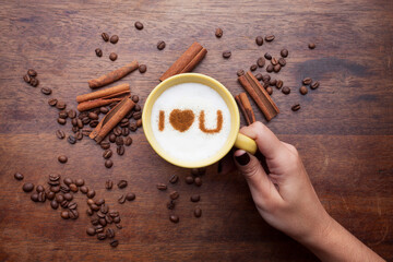 A retro cup with coffee cream. Food art creative concept image, cute drawing with cinnamon powder over milk cream on a wooden background.