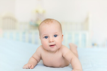 Cute adorable caucasian little 5 month old infant baby boy lying on tummy at nursery bed room having fun playing and smiling. Happy healthy newborn child concept. Funny toddler kid closeup portrait