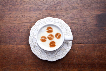 A retro cup with coffee cream. Food art creative concept image, cute drawing with cinnamon powder over milk cream on a wooden background.