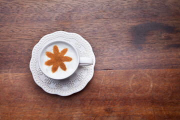 A retro cup with coffee cream. Food art creative concept image, cute drawing with cinnamon powder over milk cream on a wooden background.
