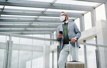 Businessman with luggage going on business trip, wearing face mask at the airport.
