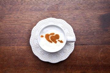 A retro cup with coffee cream. Food art creative concept image, cute drawing with cinnamon powder over milk cream on a wooden background.