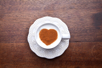 A retro cup with coffee cream. Food art creative concept image, cute drawing with cinnamon powder over milk cream on a wooden background.