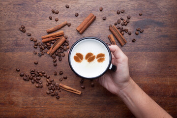 A retro cup with coffee cream. Food art creative concept image, cute drawing with cinnamon powder over milk cream on a wooden background.
