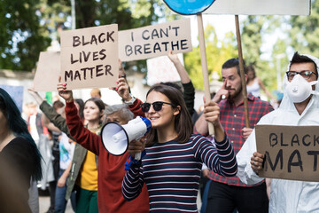 Black lives matters protesters with megaphone holding signs and marching outdoors in streets.