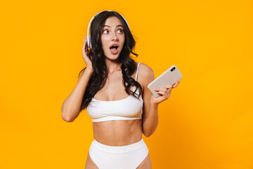 Image of surprised woman in swimsuit using cellphone and headphones