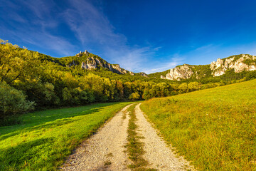 A field road through the valley of mountain landscape with rocky peaks on background in summer time. The National Nature Reserve Sulov Rocks, Slovakia, Europe.