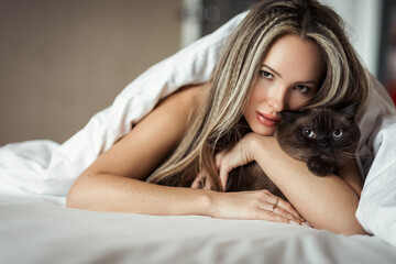Naklejka premium Close up portrait of a young beautiful girl. holds a cat in his hands. Pets. Rest at home. Lies in bed.