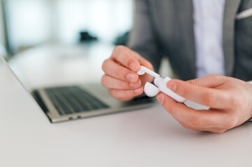 Close-up image of a businessman's hands holding wireless earphones in the office.