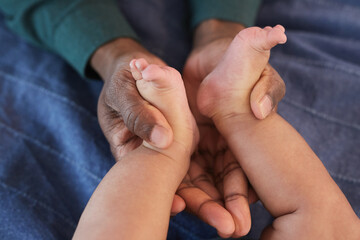 Above view close up of loving African-American father holding tiny baby feet in hands, copy space