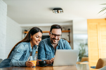 Cute couple at home sitting at table and looking at laptop.