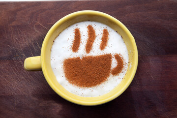 A rustic mug with coffee cream. Food art creative concept image, drawing with cinnamon powder over wooden background.