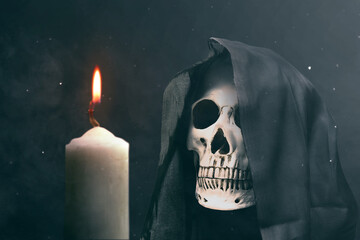 Human skull with a black cloak and burning candle on dark background