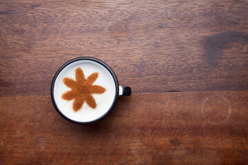 A rustic mug with coffee cream. Food art creative concept image, drawing with cinnamon powder over wooden background.