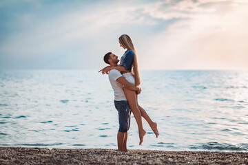 A man and a beautiful woman are enjoying their honeymoon on the beach at sunset. Husband and wife are walking by the ocean. Beautiful young couple spend time together.