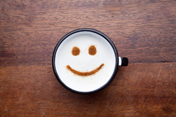 A rustic mug with coffee cream. Food art creative concept image, drawing with cinnamon powder over wooden background.