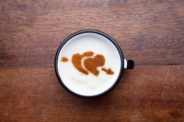 A rustic mug with coffee cream. Food art creative concept image, drawing with cinnamon powder over wooden background.