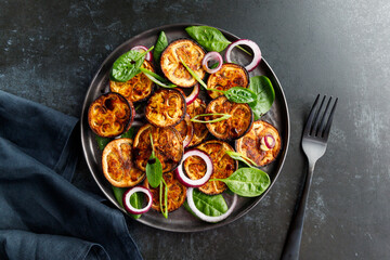 Salad with grilled eggplant, spinach, purple onion and sauce on a dark table.