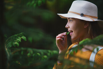 Young woman on a walk outdoors in forest in summer nature, eating spruce shoots.
