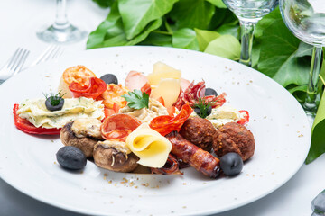 Wedding appetizer made by mushroom, cheese, olives, pepper, meatballs, fried bacon, sausage slices on round plate