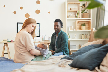 Obraz premium Portrait of modern interracial family with African-American father working from home and Caucasian mother holding baby, copy space