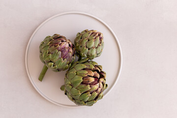 Obraz premium Minimalistic image ofartichokes in a white plate on a light gray