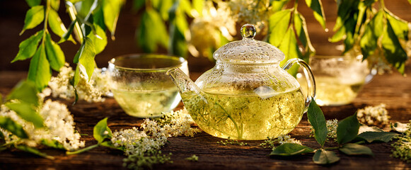 Elderflower tea infusion of elder white flowers in a glass teapot on a wooden table. Healthy and delicious herbal drink  - obrazy, fototapety, plakaty