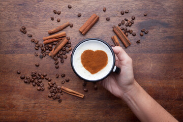 A rustic mug with coffee cream. Food art creative concept image, drawing with cinnamon powder over wooden background.
