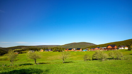 Fototapeta na wymiar Small village of mountain huts in a green colorful hilly landscape with Snezka mountain in the background, Pomezni Boudy, Krkonose mountains, Czech Republic, Poland