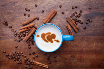 A rustic mug with coffee cream. Food art creative concept image, drawing with cinnamon powder over wooden background.
