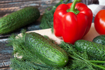 vegetables, Bulgarian peppers, dill, cucumbers on a light cutting Board, dark wooden background
