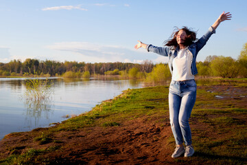 Girl or woman jumping on the shore or beach of the lake in the evening at sunset.