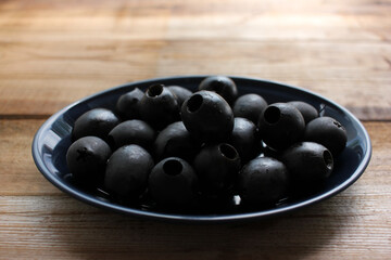 Bowl of black olives. Black canned pitted olives in a dark blue glass bowl on a rustic wooden table. Close-up, selective focus