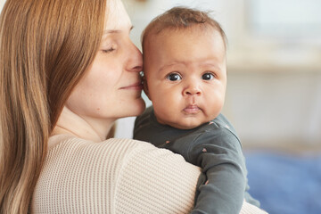 Close up portrait of mature Caucasian mother holding cute mixed-race baby looking at camera, copy...