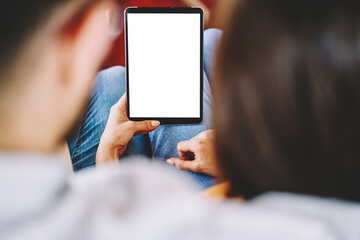 Cropped back view of couple in love watching video online on touch pad with blank screen area for internet advertisement using wireless 4G connection.Selective focus on digital tablet with copy space