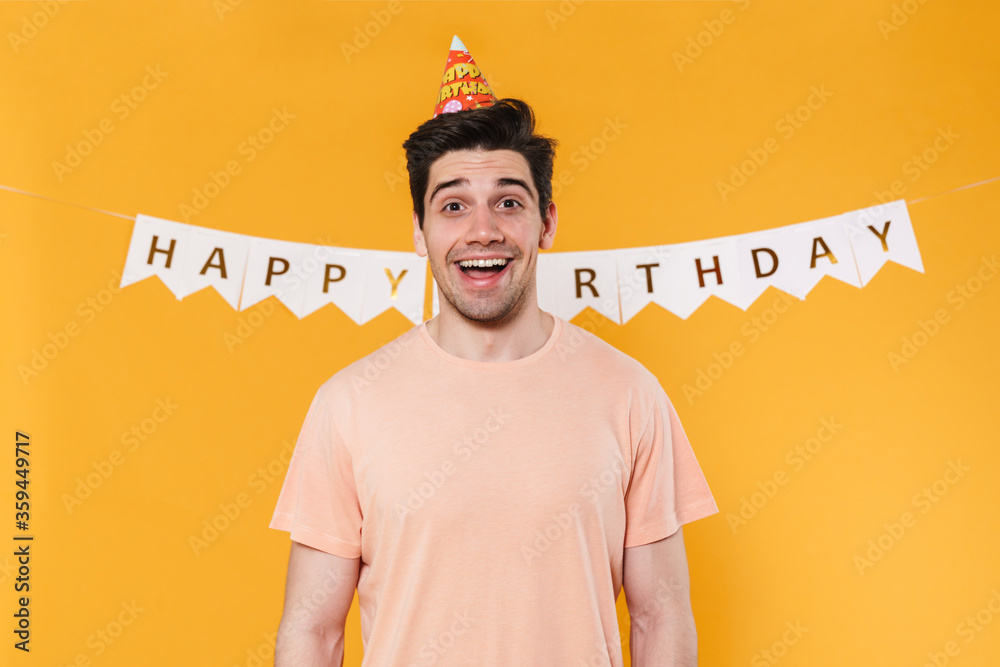 Canvas Prints Photo of excited young man in party cone posing and smiling at camera