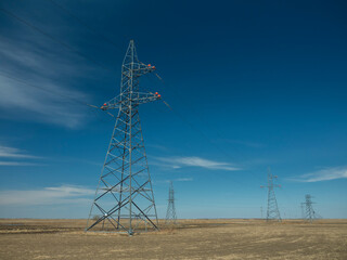 Front view of a line of metal poles of a high voltage power line with red plastic circles at the top.