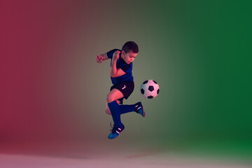 Fototapeta na wymiar Leader. Teen male football or soccer player on gradient background in neon light. Caucasian boy training, practicing on the run, in jump. Concept of sport, competition, winning, motion, action.
